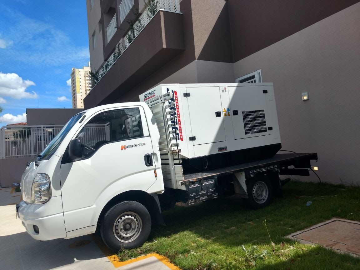 Caminhão com gerador estacionado em área arborizada ao lado de shopping