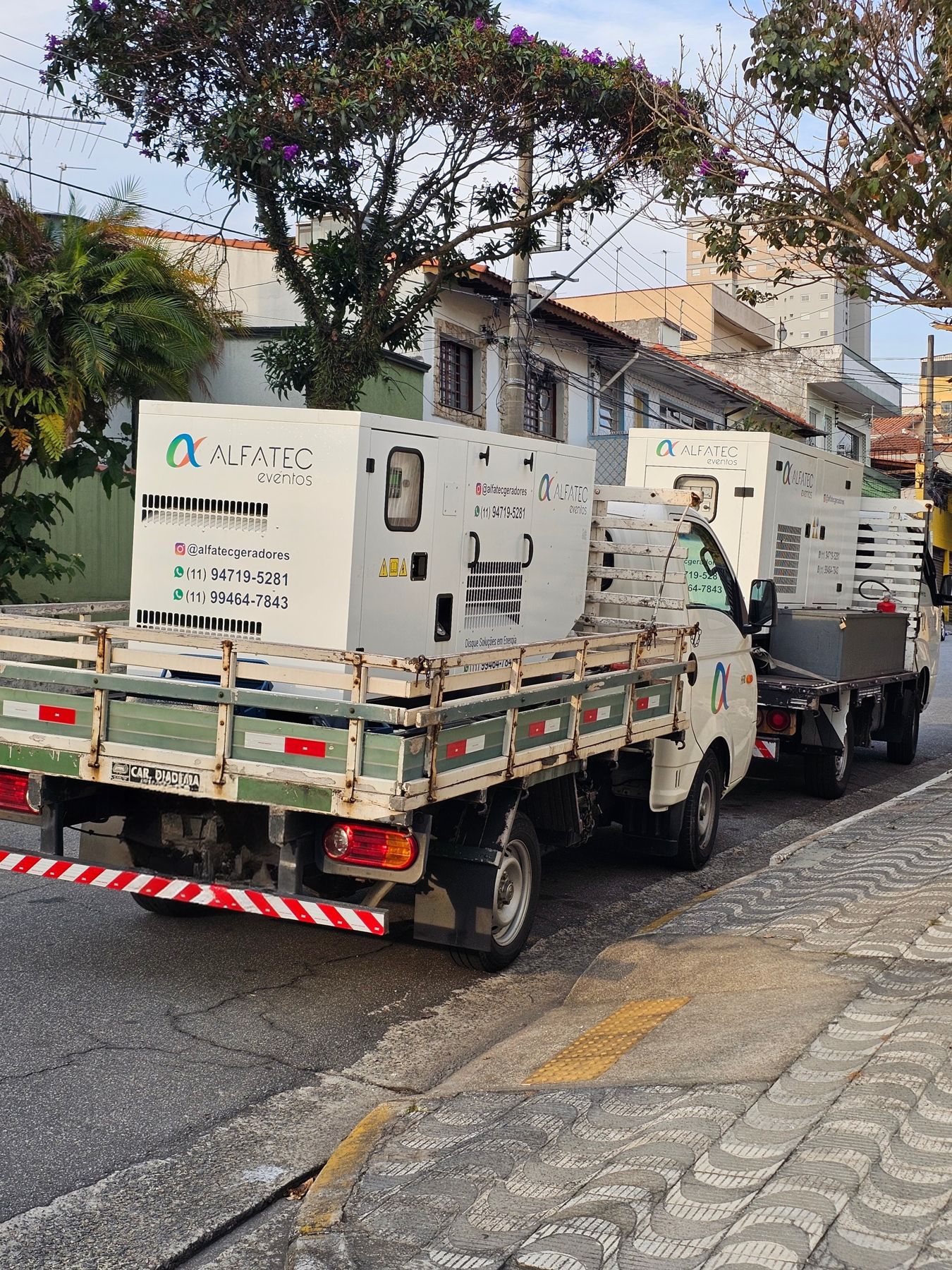 Dois caminhões da Alfatec com geradores estacionados em rua residencial